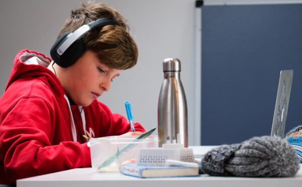 En gutt med hodetelefoner og rød genser sitter og jobber konsentrert ved et skrivebord.